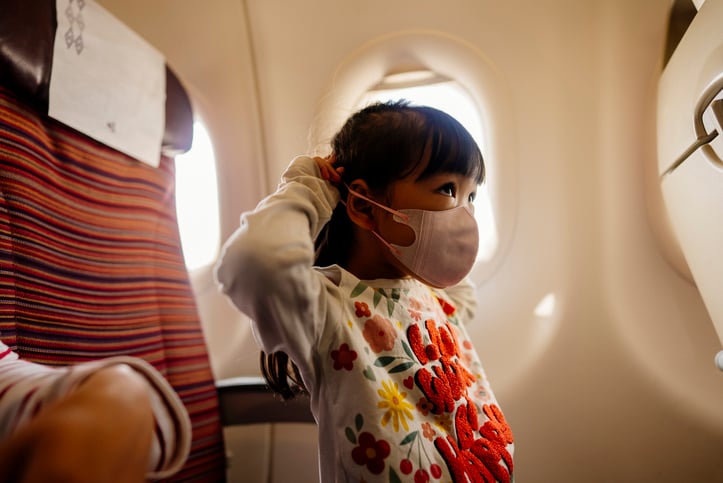 A children covering her face with a face mask in an airplane