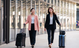 Two young female travelers walking with wheeled luggage at airport terminal.jpg