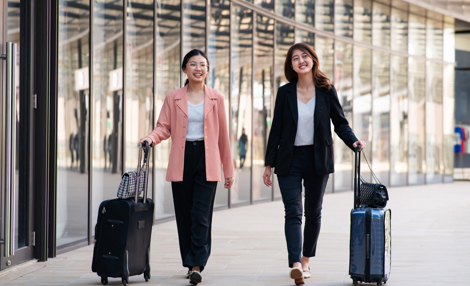 Two young female travelers walking with wheeled luggage at airport terminal.jpg
