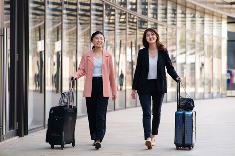 Two young female travelers walking with wheeled luggage at airport terminal.jpg