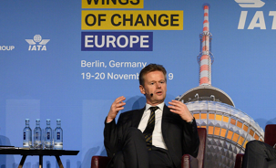 Peter Gerber sitting on stage with a backdrop of Wings of Change Europe event in 2019