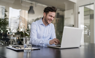 Smiling businessman using laptop at desk in office.jpg