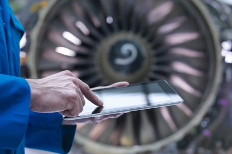 Aircraft engineer using a tablet with a commercial aircraft engine in the background.