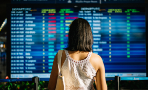 Asiatische Touristin, die sich die Ankunftsabflugtafel am Flughafen ansieht.jpg