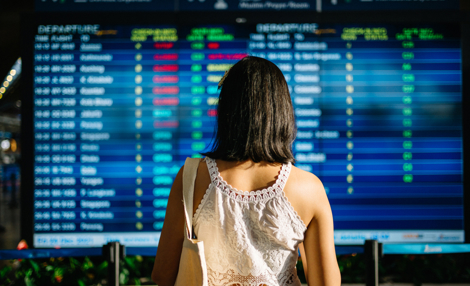 Asiatische Touristin, die sich die Ankunftsabflugtafel am Flughafen ansieht.jpg