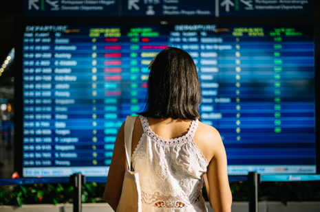 Asiatische Touristin, die sich die Ankunftsabflugtafel am Flughafen ansieht.jpg