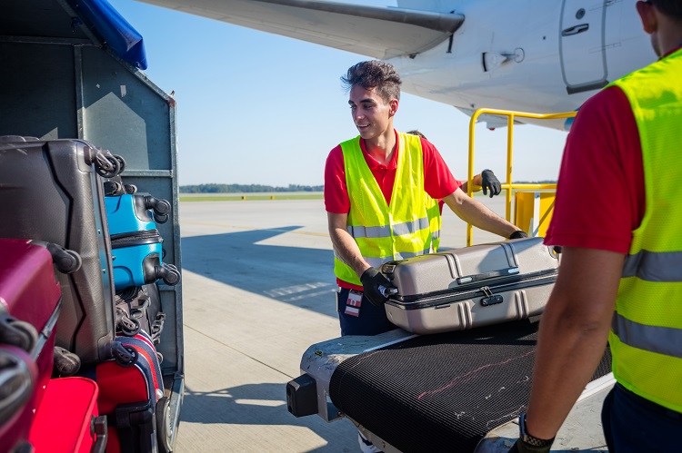 Airport ground handlers loading suitcases onto an aircraft conveyor